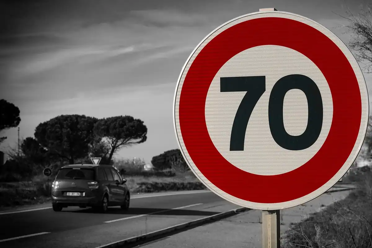 Indicator rutier cu limită de viteză de 70 și o mașină pe șosea, alb-negru