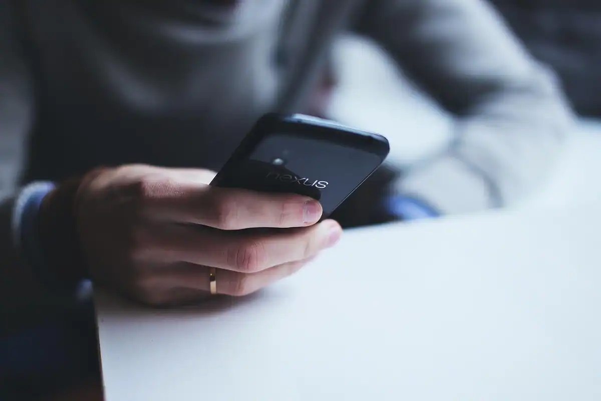 Mână care ține un telefon mobil cu ecranul aprins pe o suprafață albă