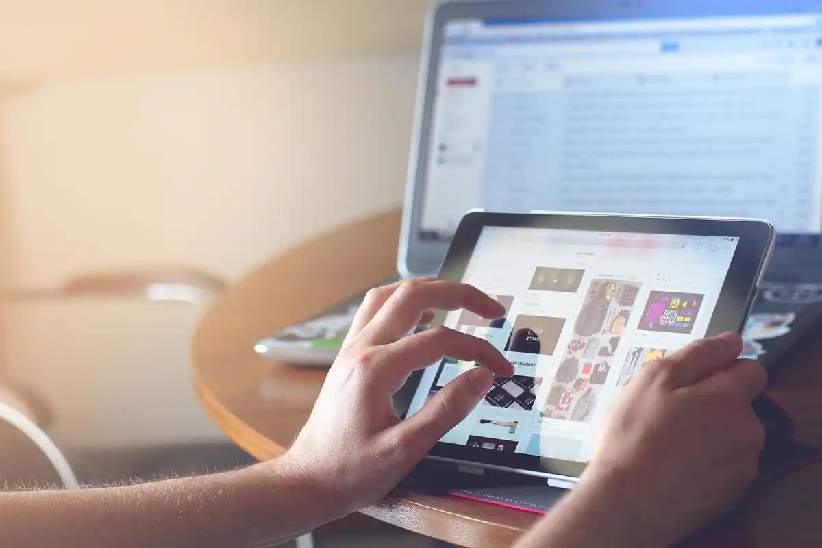 Mâini care navighează pe o tabletă cu pagini de magazin online deschise