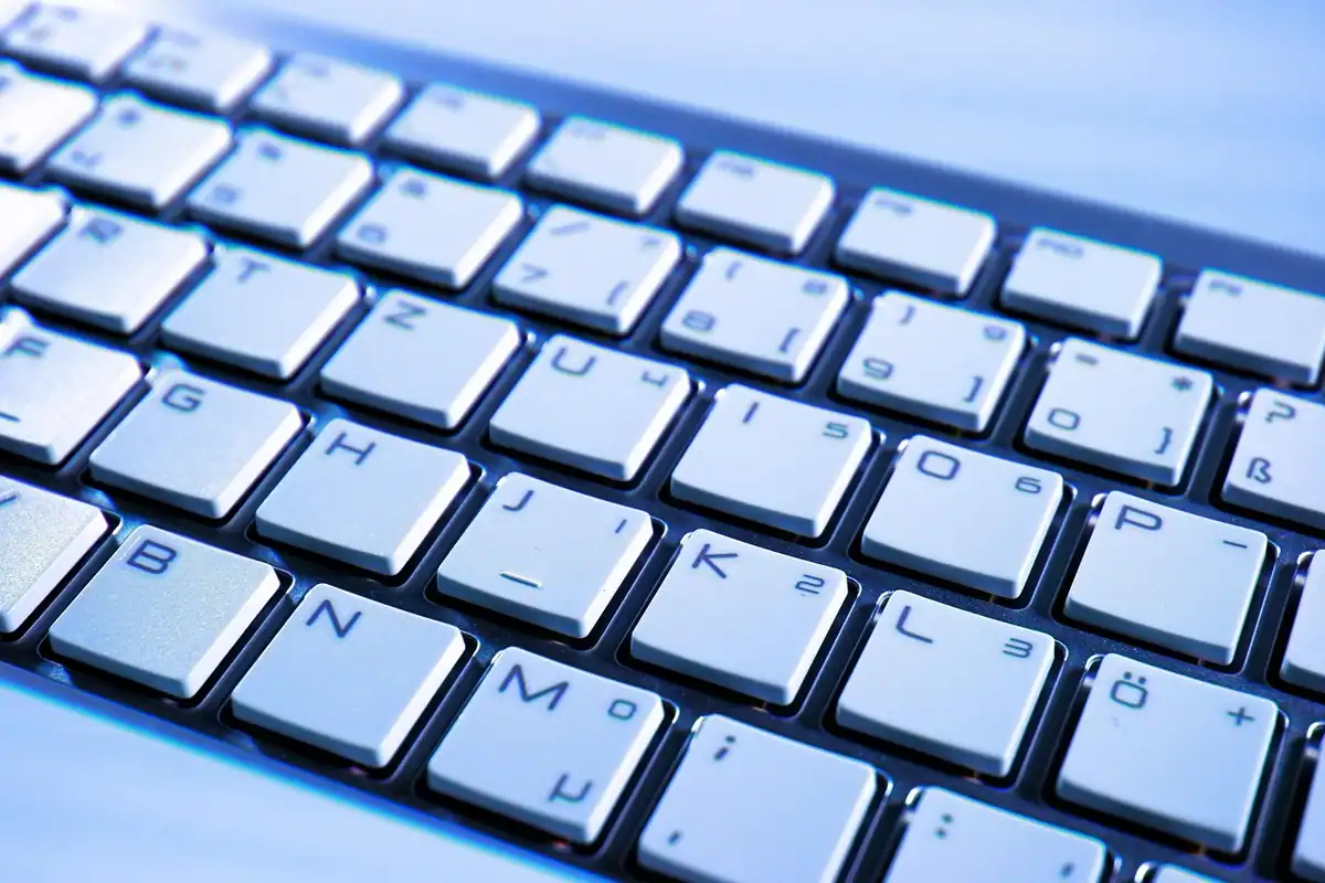 Tastatură de laptop cu taste albe, fotografiată de aproape în lumină albastră