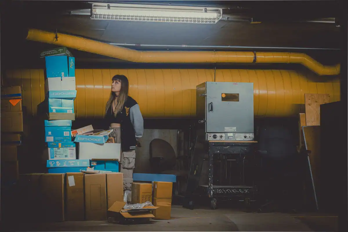 Femeie într-un depozit slab luminat, între stive de cutii de carton