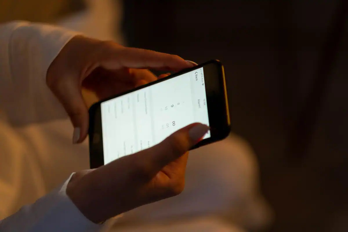 Mâini care țin un telefon cu pagina de setări deschisă, într-o încăpere întunecată