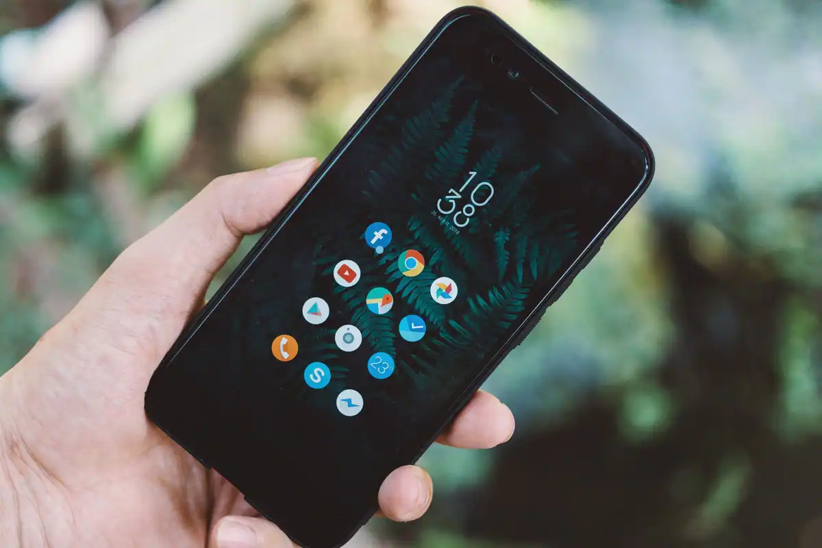 Mână care ține un smartphone cu pictogramele aplicațiilor afișate pe ecran