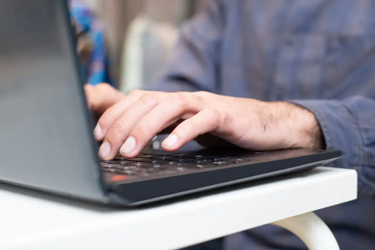 Mâini care tastează pe tastatura unui laptop, într-un spațiu de lucru ordonat