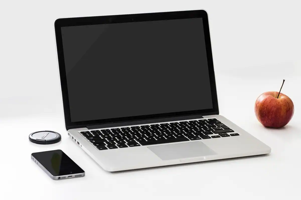 Laptop deschis, măr, ceas și telefon așezate pe un fundal alb