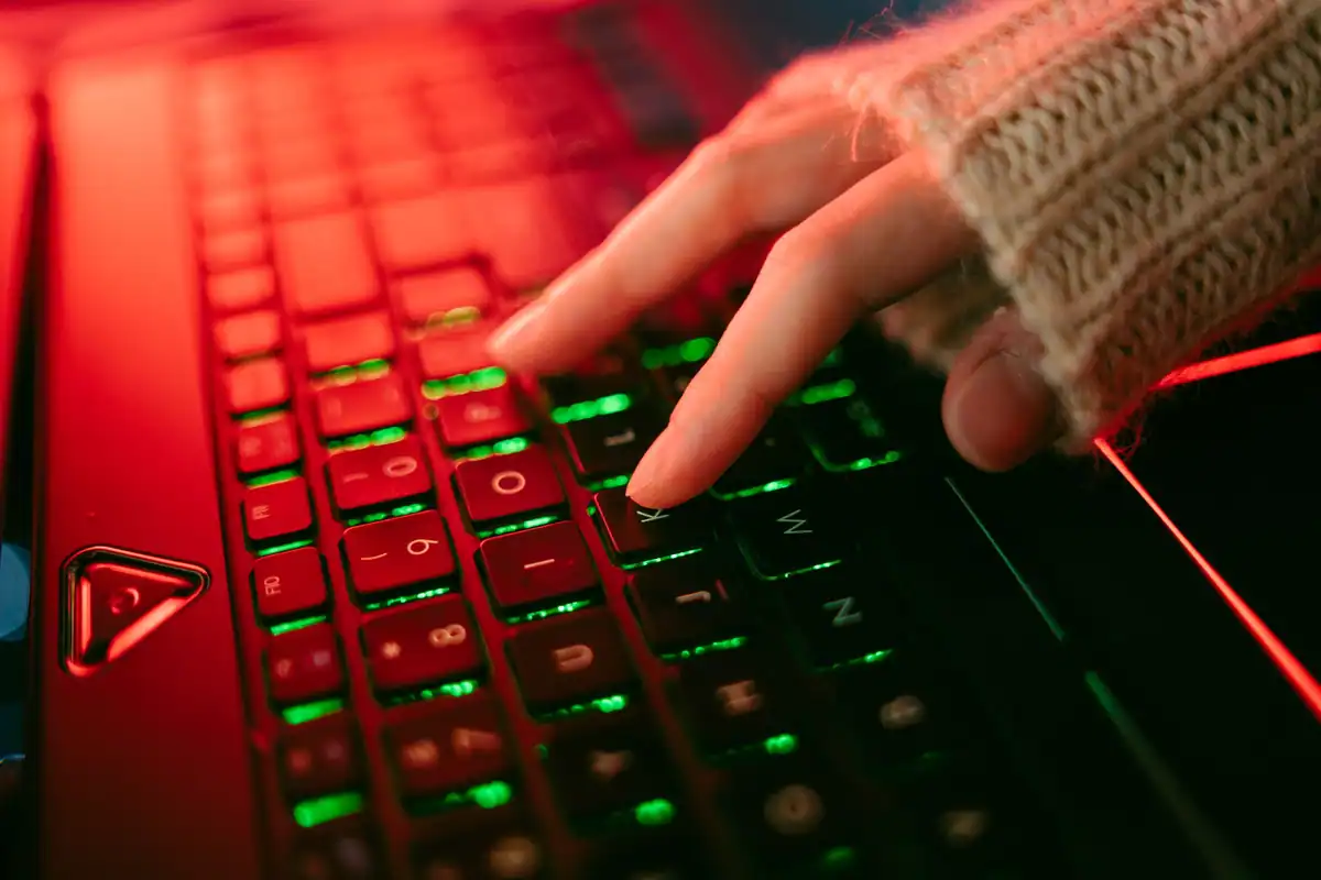 Deget care apasă o tastă de laptop, pe o tastatură iluminată în roșu