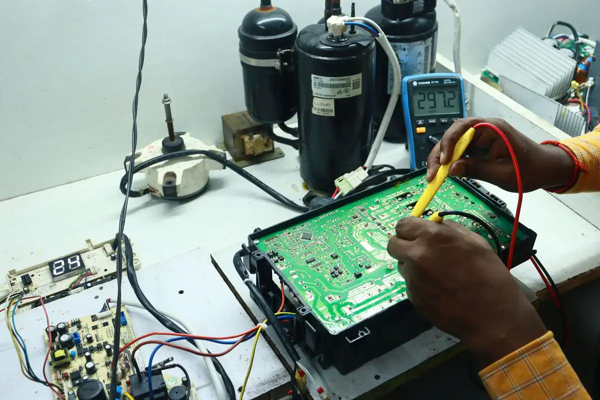 Tehnician care testează cu multimetrul o placă electronică verde de aparat