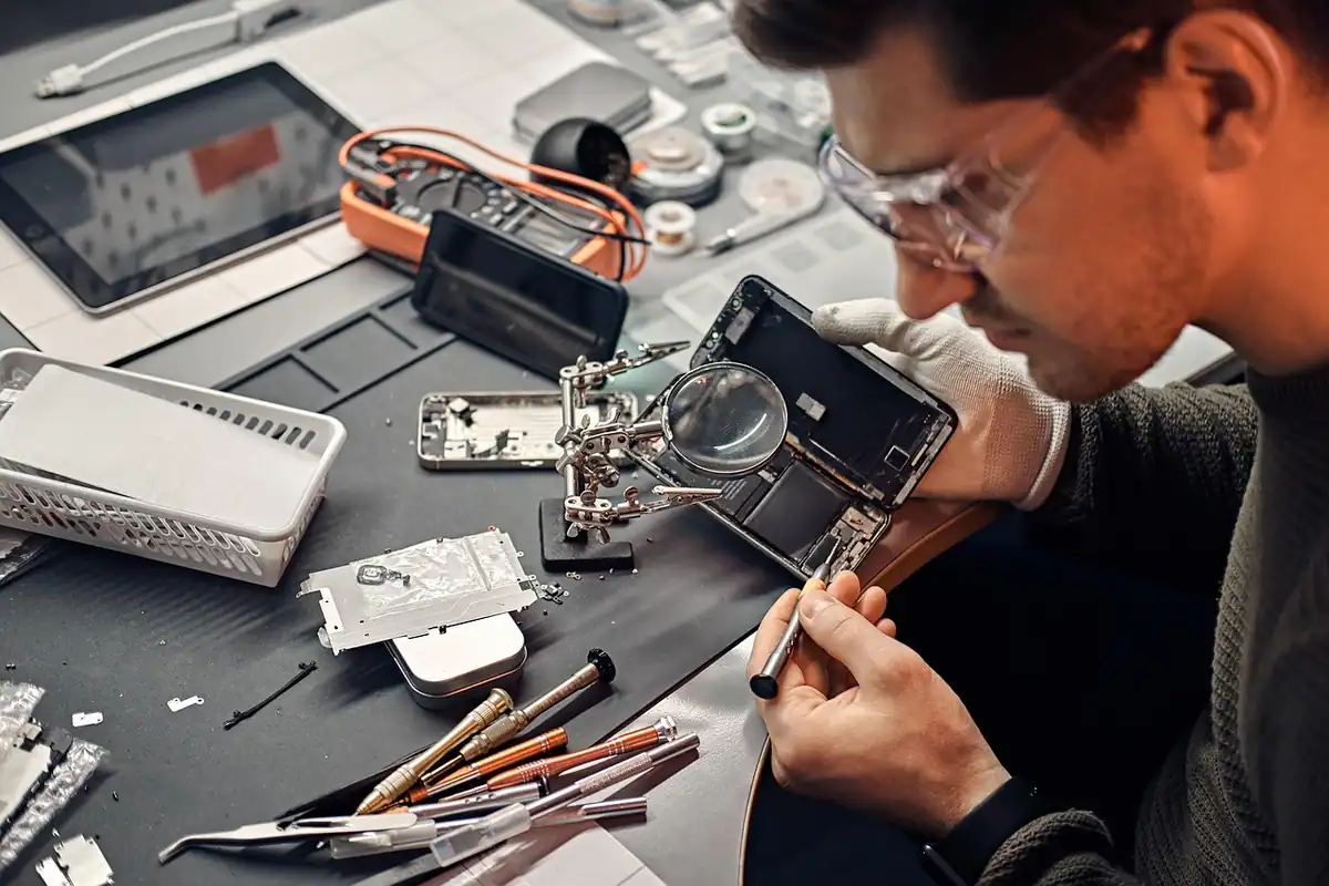 Tehnician la masa de lucru, reparând un dispozitiv electronic aflat în garanție