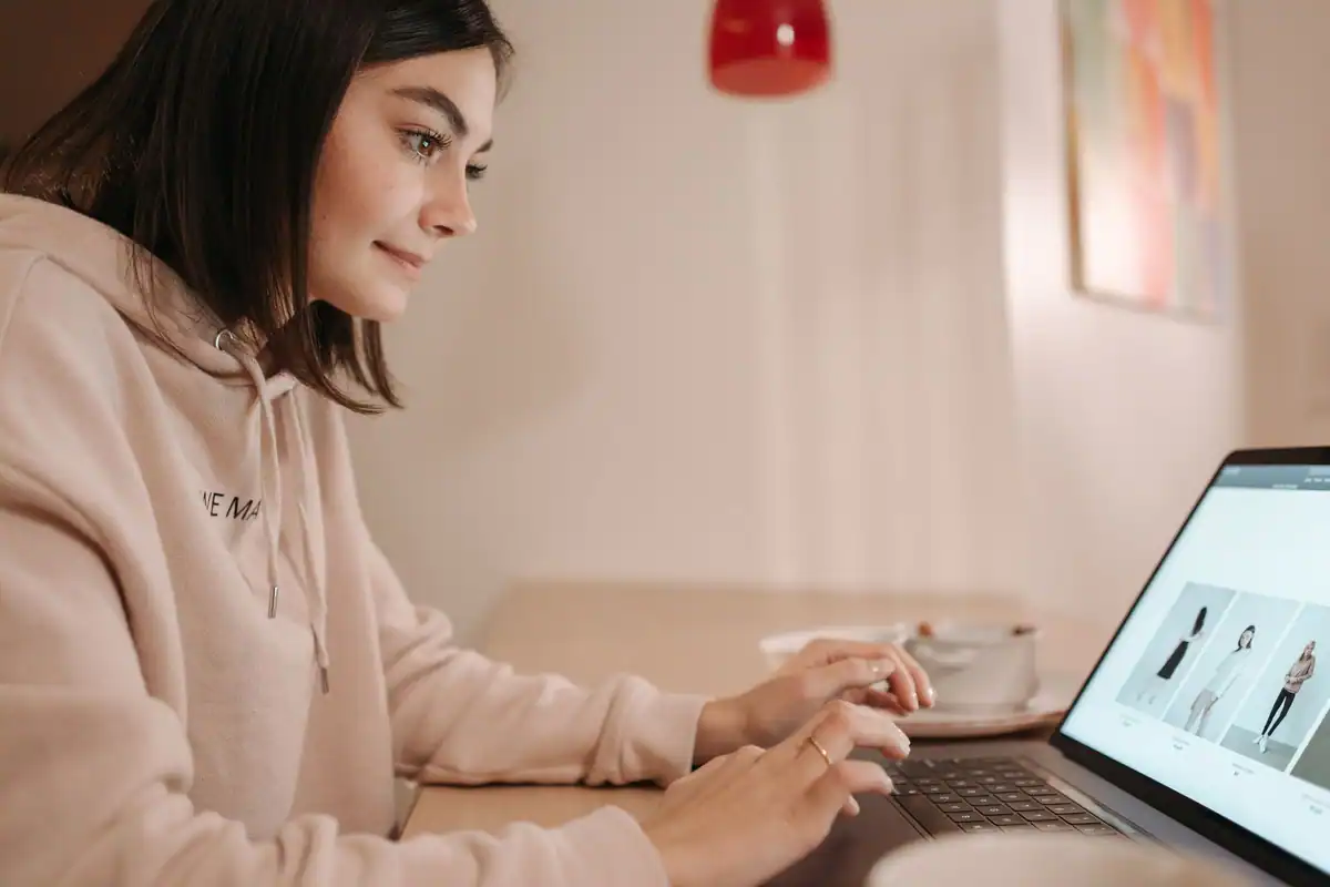 Tânără în hanorac roz care răsfoiește un magazin online pe laptop