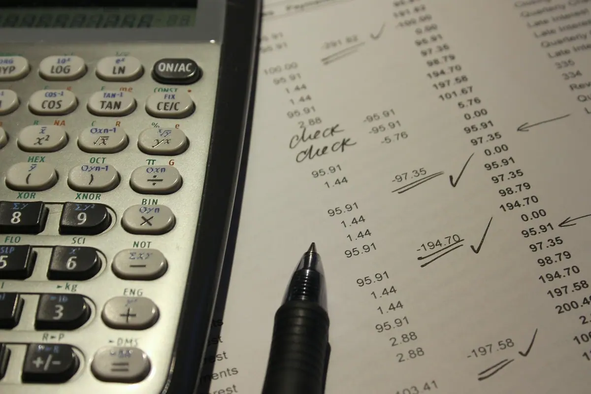 Calculator de birou lângă o listă tipărită cu sume bifate și un pix