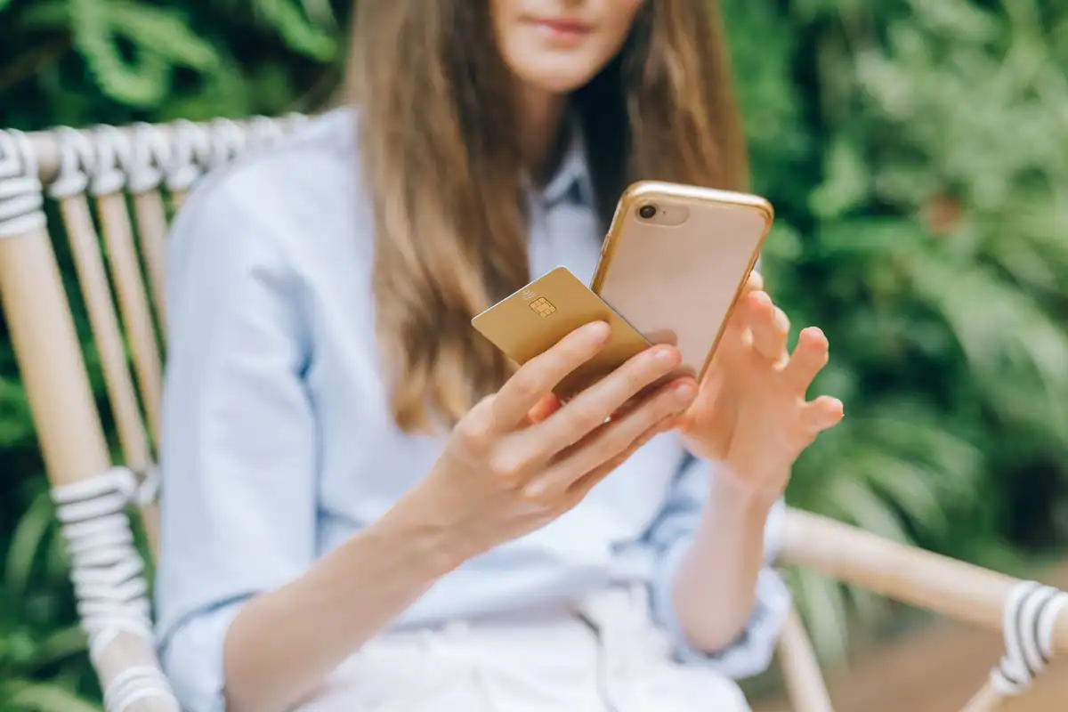 Femeie care folosește telefonul, ținând în mână un card bancar