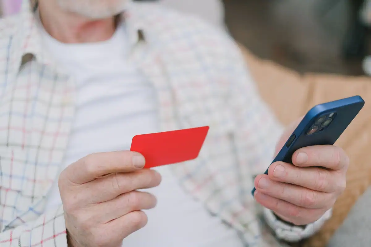 Persoană în vârstă care ține un card roșu lângă telefonul mobil