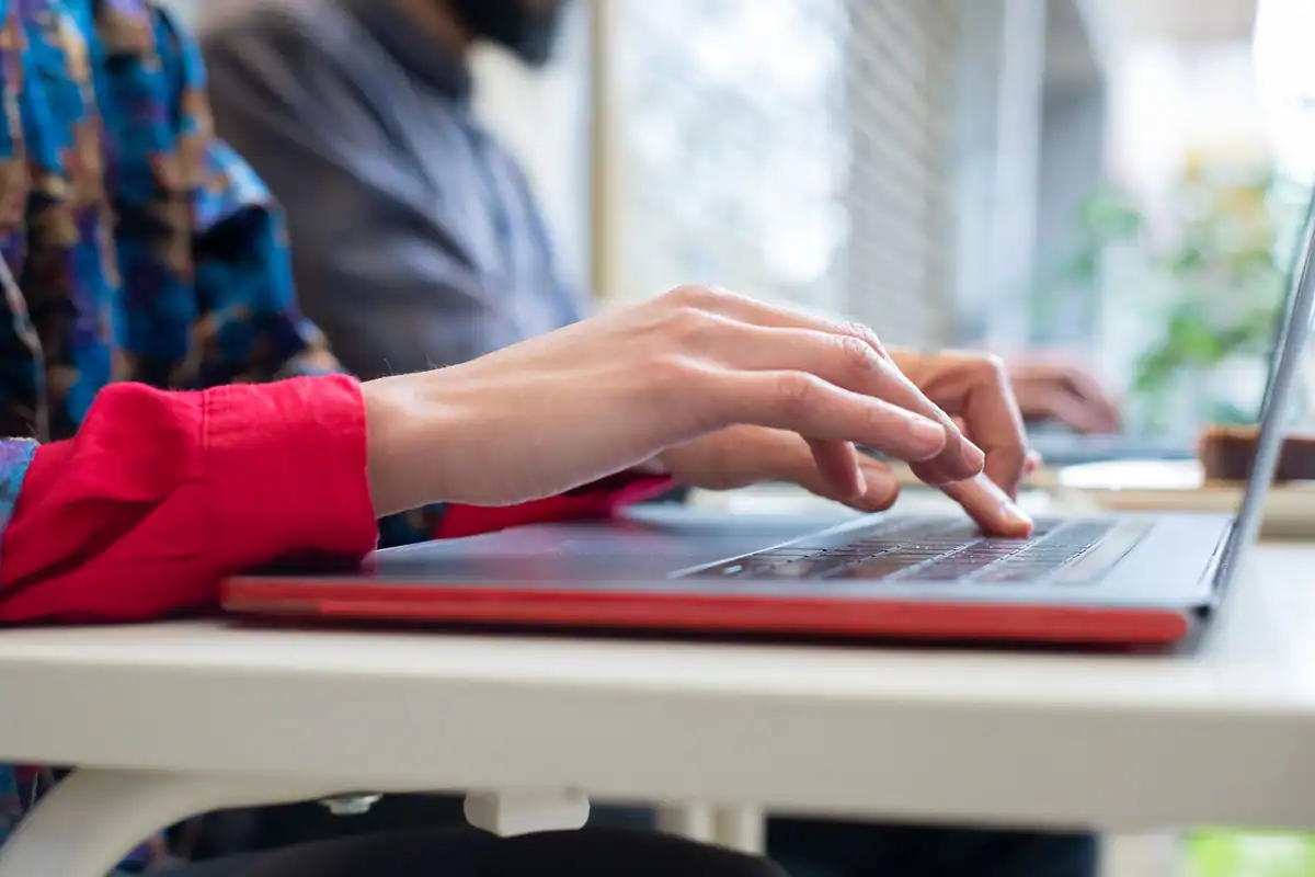 Mâini care tastează pe un laptop așezat pe o masă albă