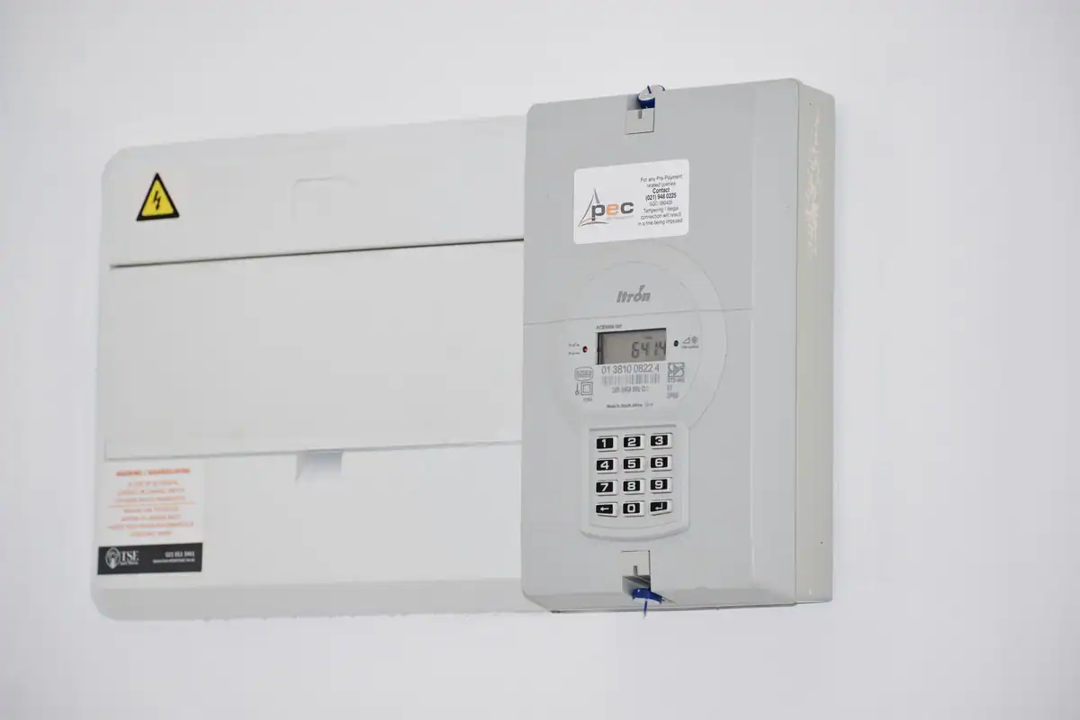 Contor electric montat pe un perete alb, lângă tabloul de siguranțe